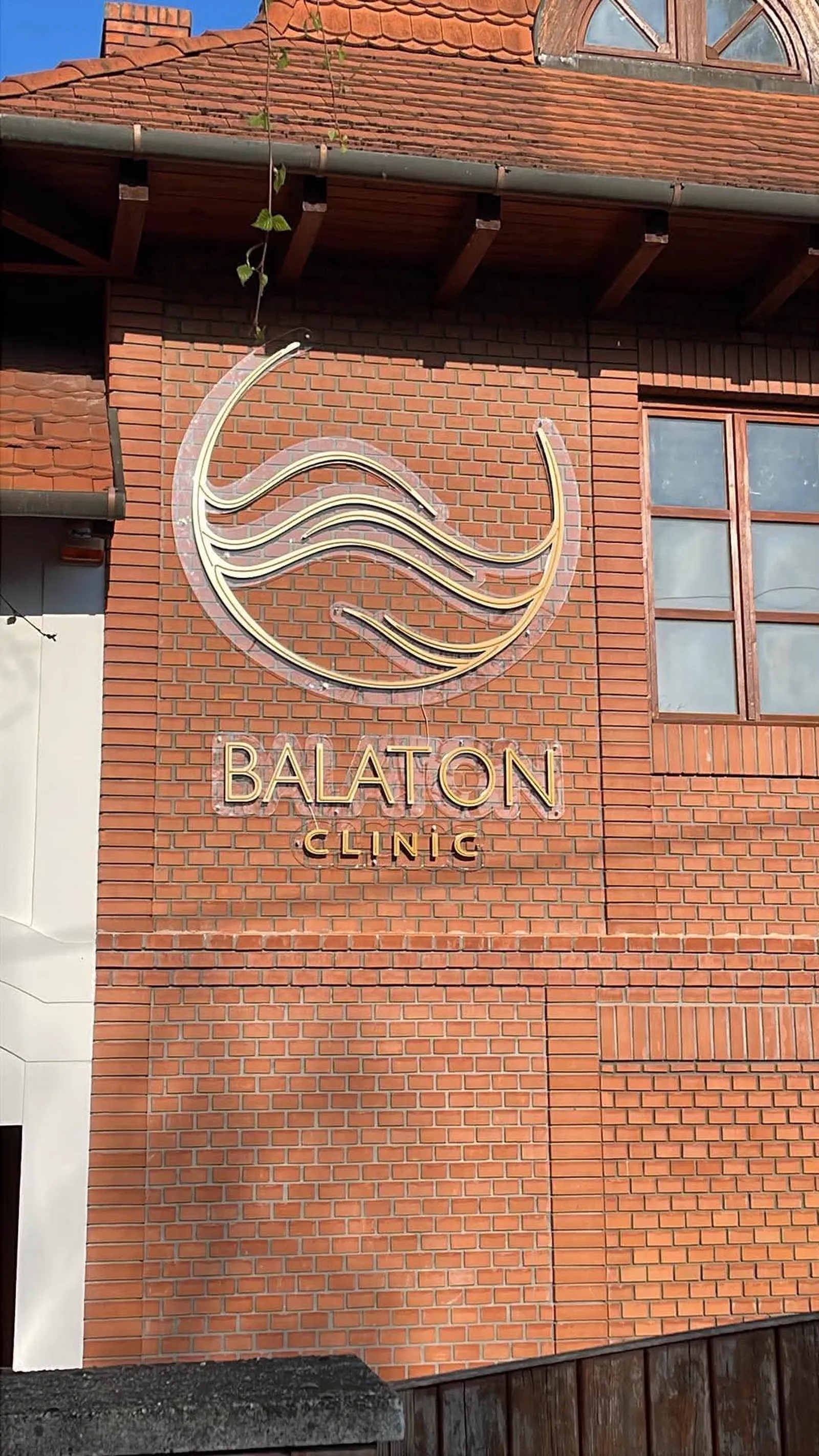 Balaton Clinic világító logó nappali fényben, téglahomlokzaton